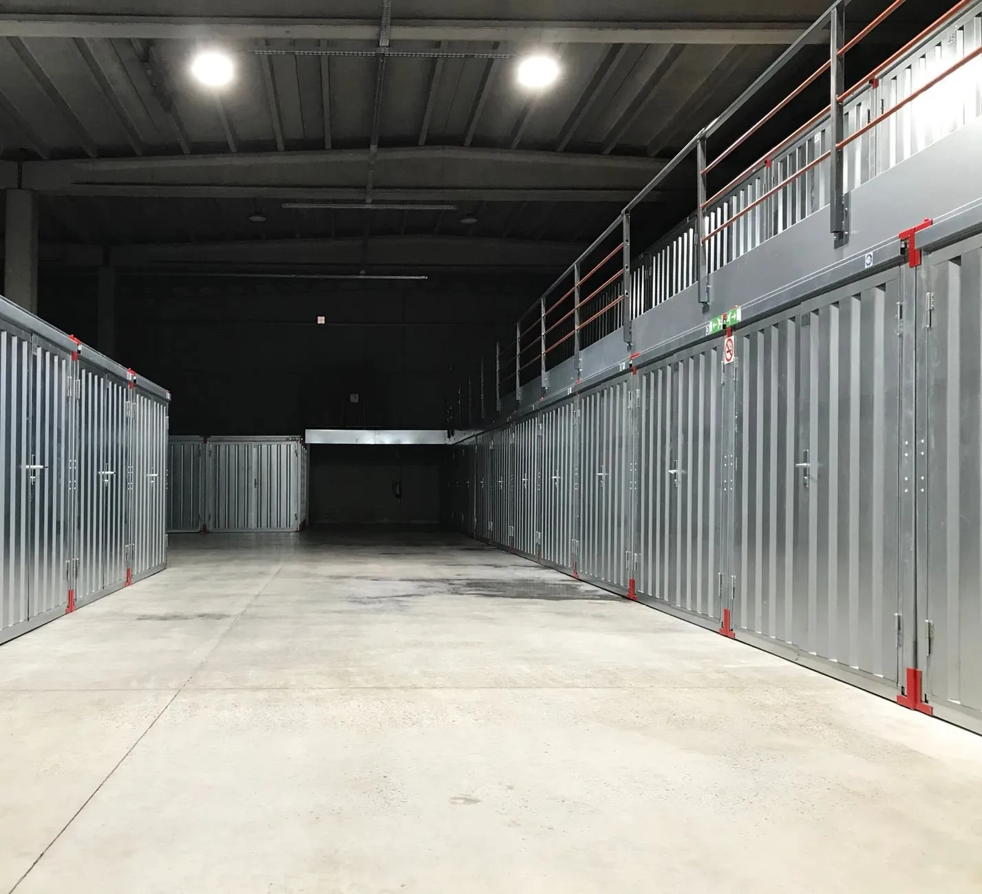 A long lit corridor of grey steel storage units with a walkway above on the right