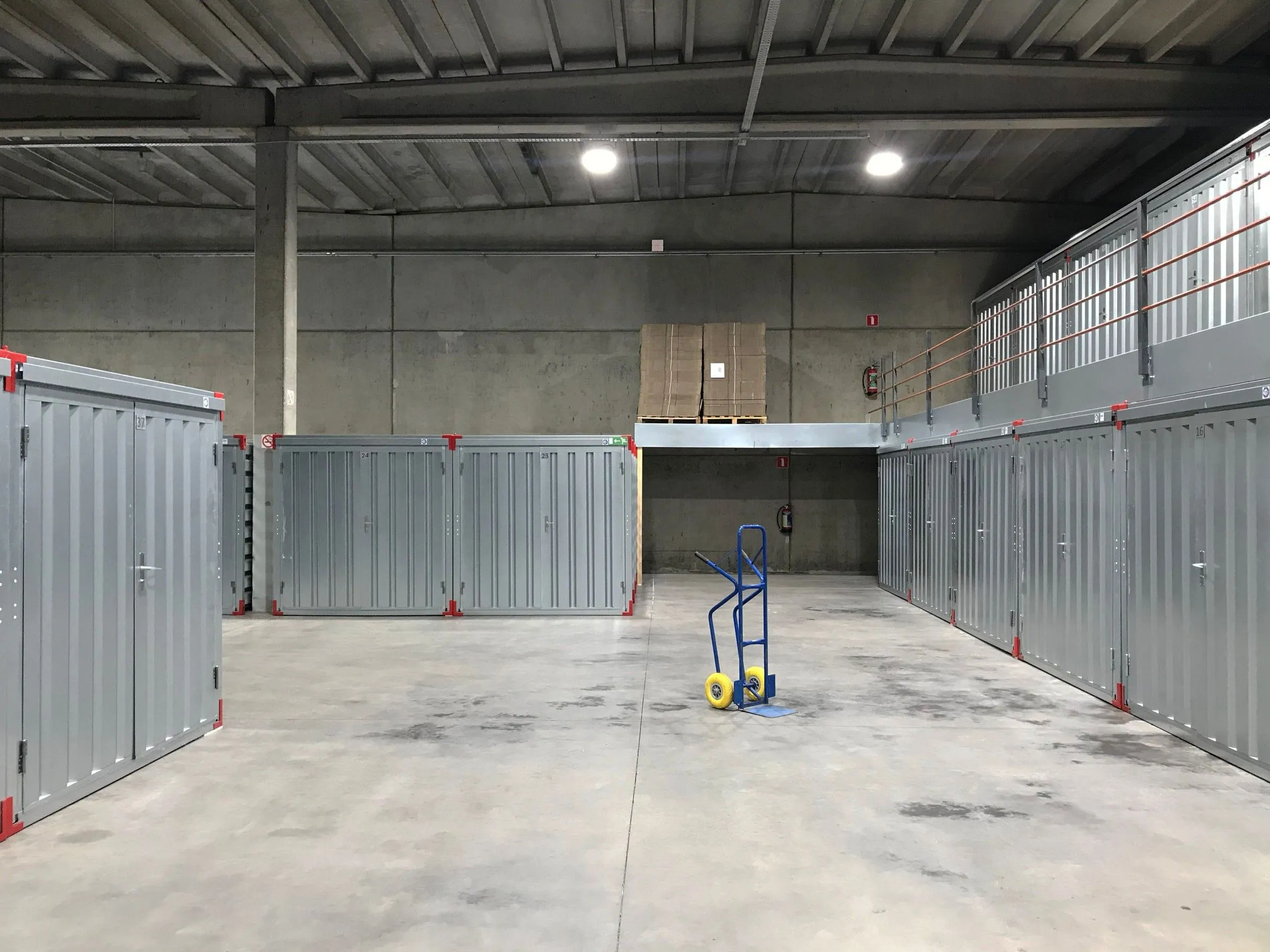Grey steel storage units lining a clean, lit warehouse hall, with a blue hand truck waiting in the aisle