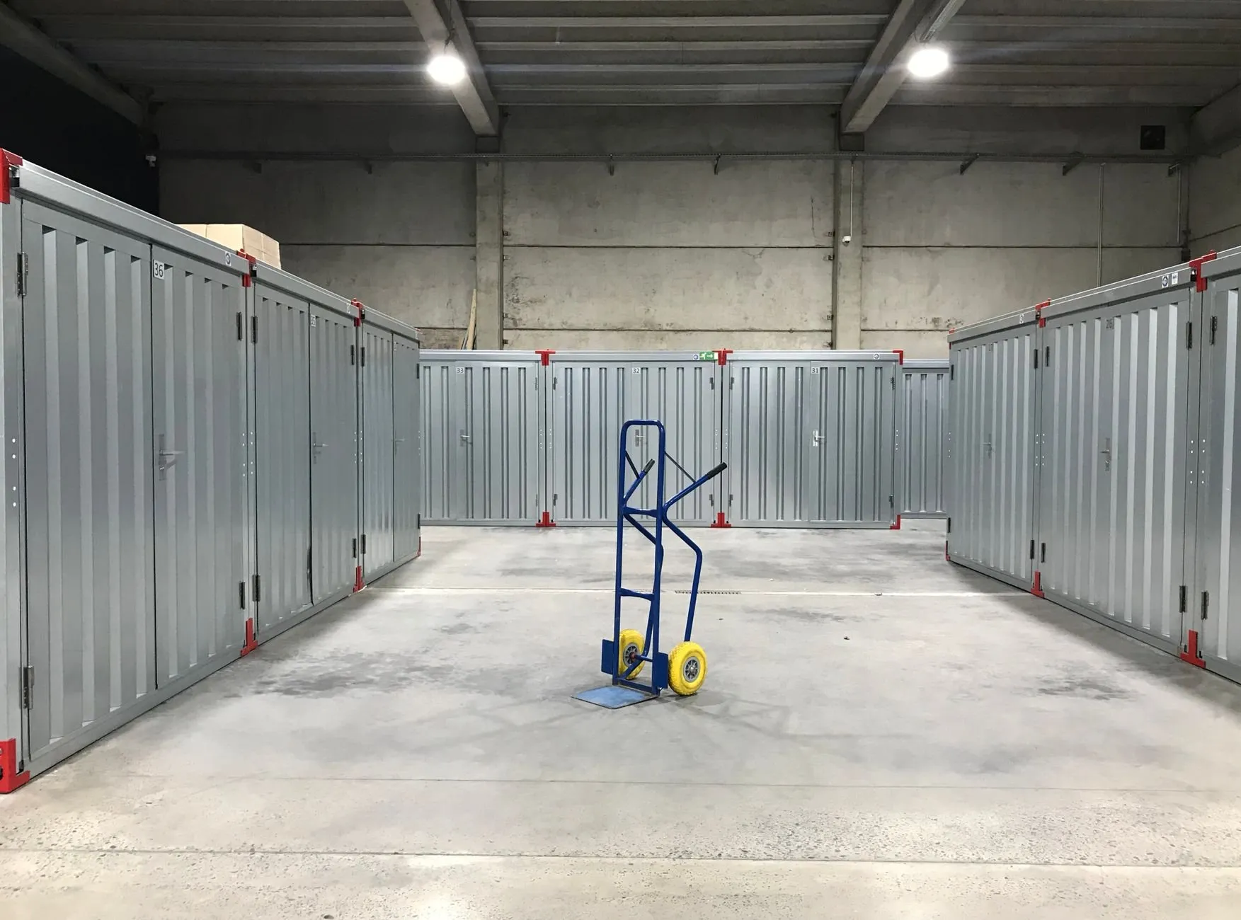 Rows of grey steel storage units in a clean warehouse hall with a hand truck in the aisle