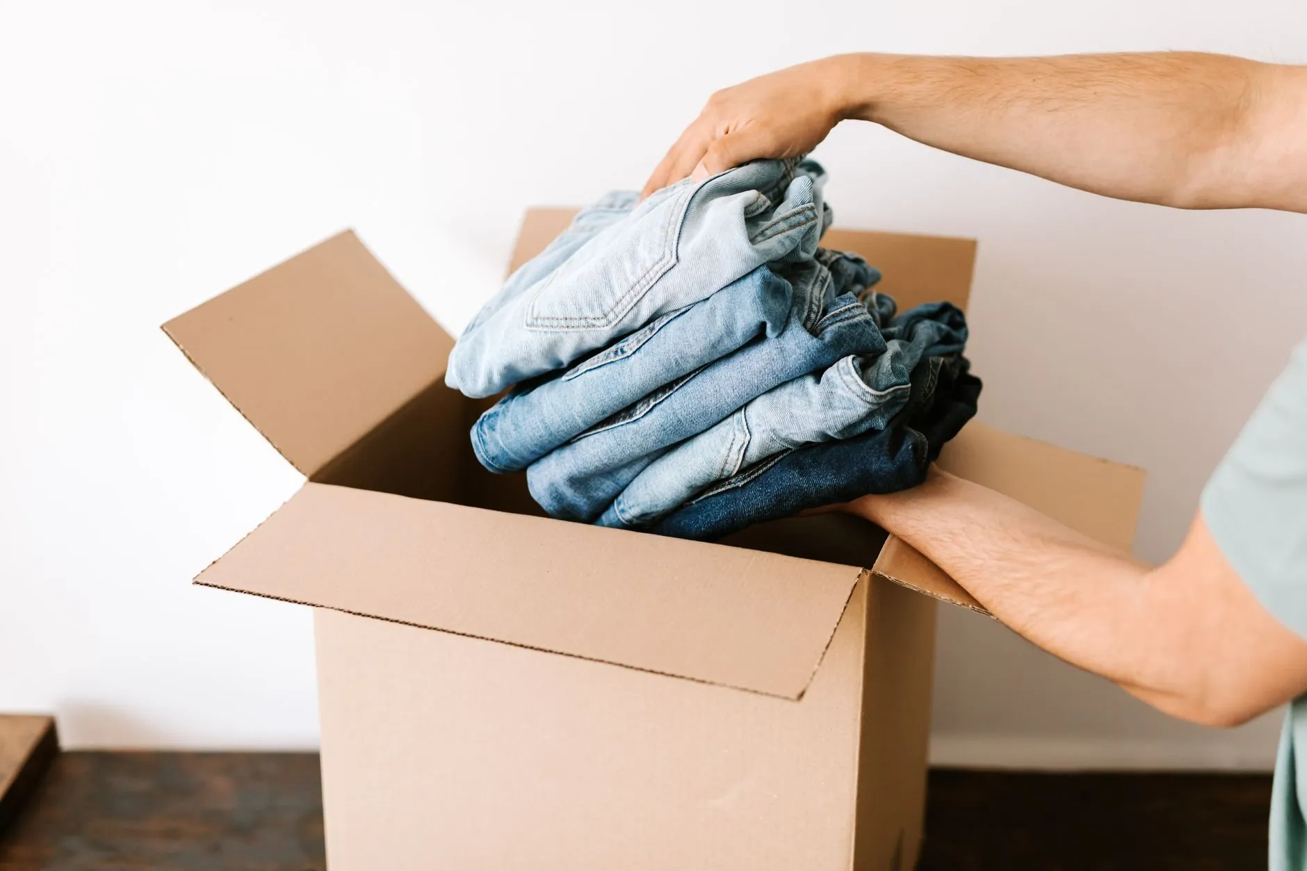 Hands packing a pile of folded jeans into an open cardboard box